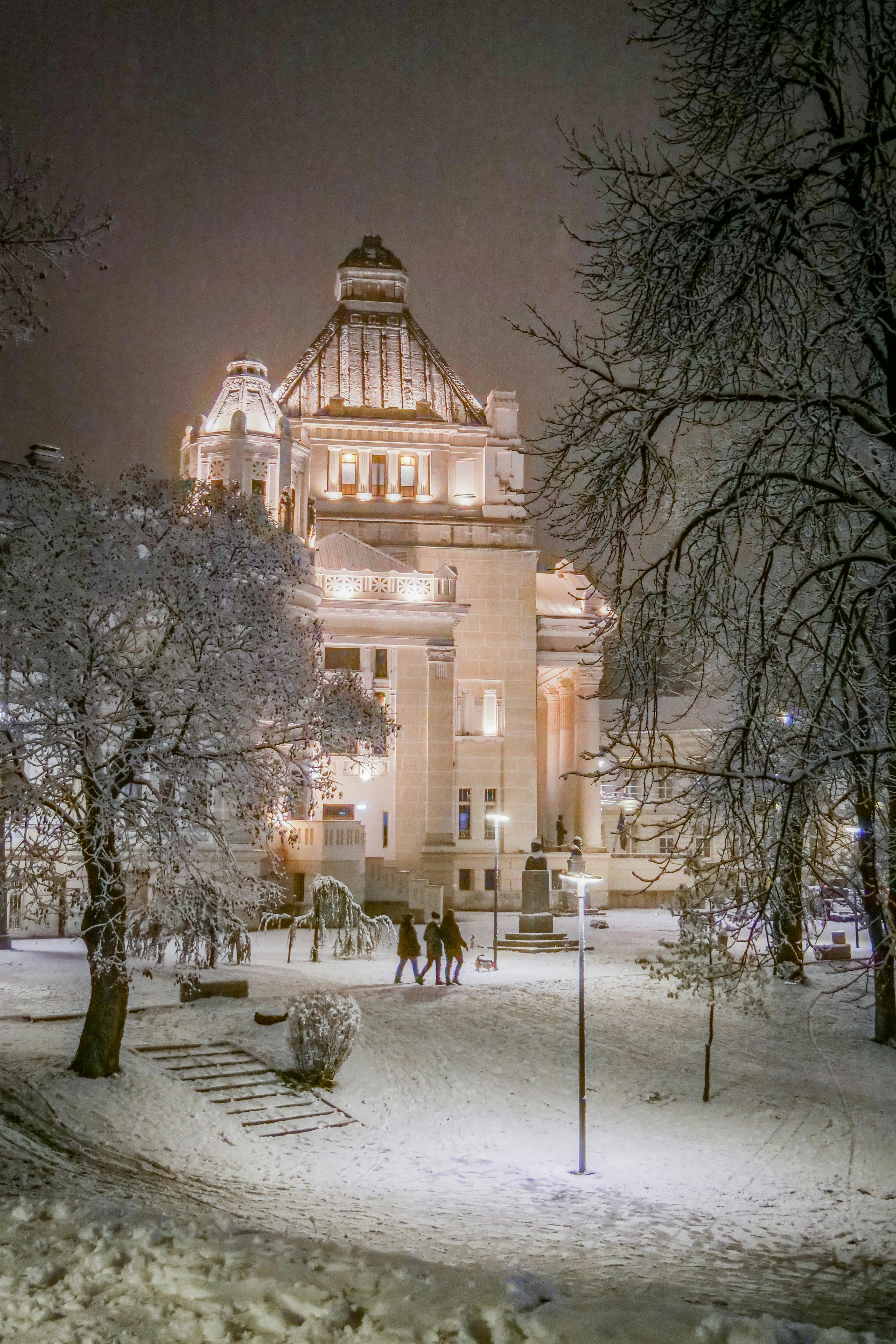 Snow-covered evening at a brightly lit architectural landmark in Arad, Romania.