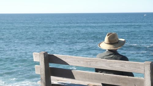 Free Man sitting on bench with hat overlooking ocean view in San Diego, California. Stock Photo