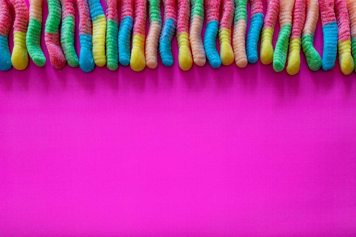 A bright and playful arrangement of gummy worms on a pink flat lay, perfect for candy lovers.
