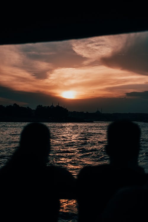 Silhouette of People Standing Near the Body of Water during Sunset