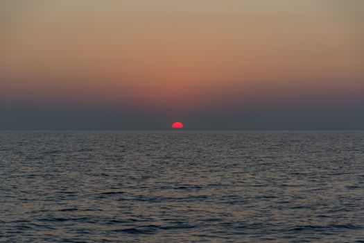 A tranquil ocean view at sunset with vivid red and orange hues in the sky.