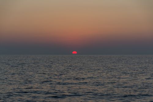 Free A tranquil ocean view at sunset with vivid red and orange hues in the sky. Stock Photo