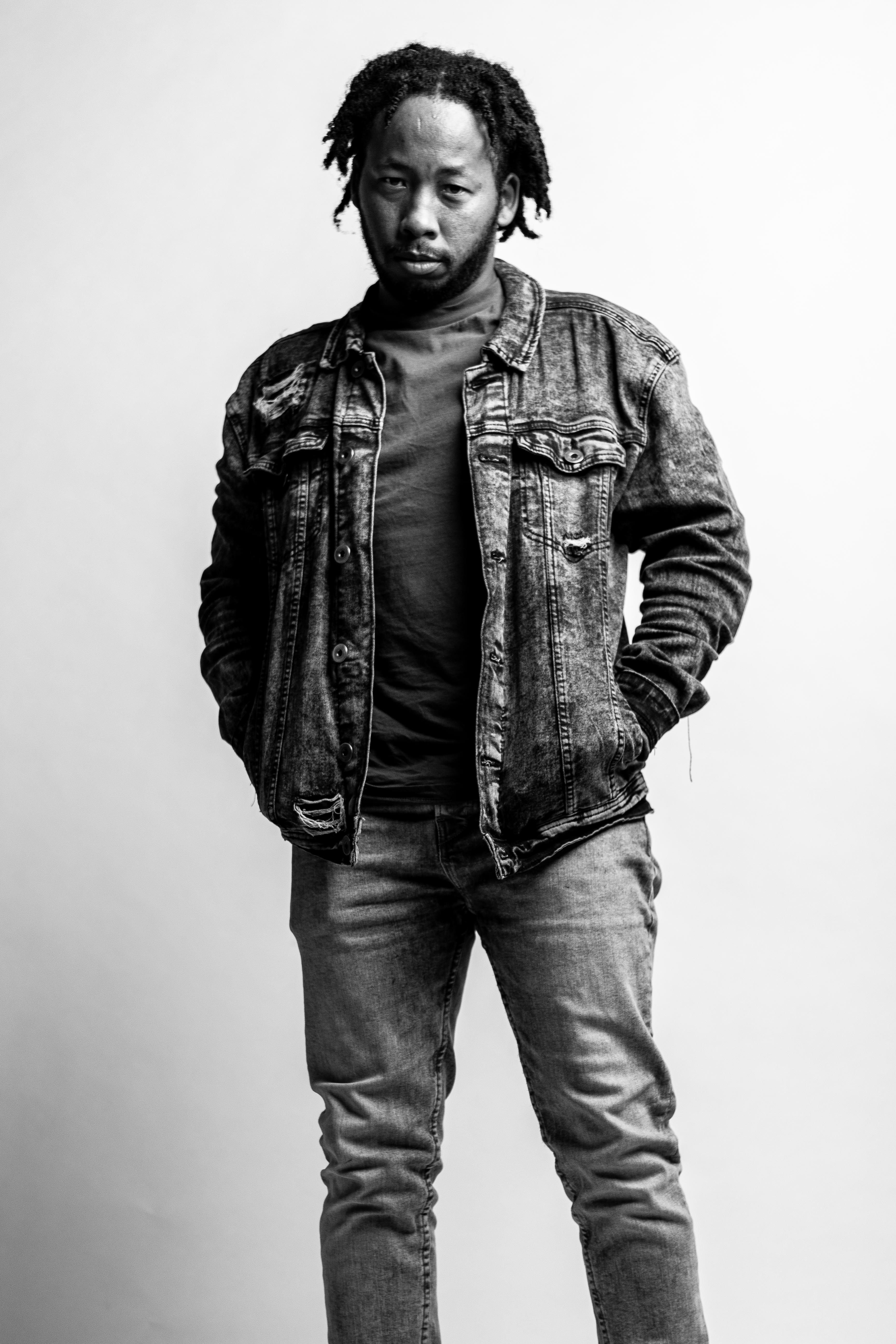 Black and white portrait of a man in denim with hands in pockets, studio setting.