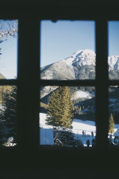 Scenic winter landscape of Vysoké Tatry, Slovakia, seen through a window, capturing snowy mountains and pine trees.