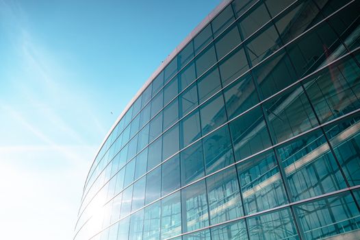A low-angle view of a modern glass office building against a clear blue sky.