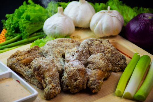 Close-up of seasoned chicken wings with fresh garlic, onions, and greens on a wooden board.