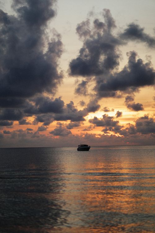 Free A tranquil ocean scene at sunset with a boat silhouette against a vibrant sky. Stock Photo