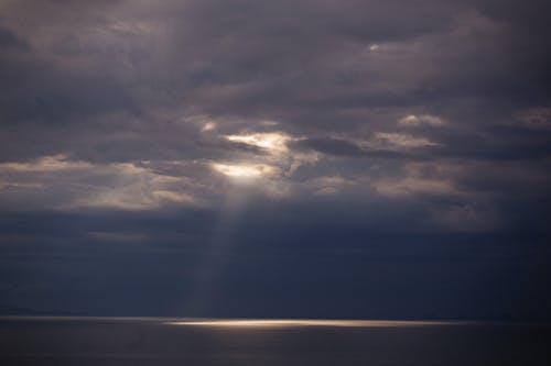 Free Ray of Sun Shining From Behind Dark Clouds onto the Sea  Stock Photo