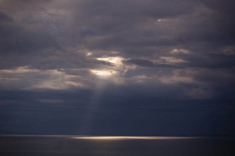 Ray Of Sun Shining From Behind Dark Clouds Onto The Sea 