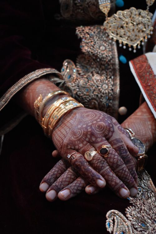 Free Close-up of intricately hennaed hands with gold bangles and rings against embellished fabric. Stock Photo