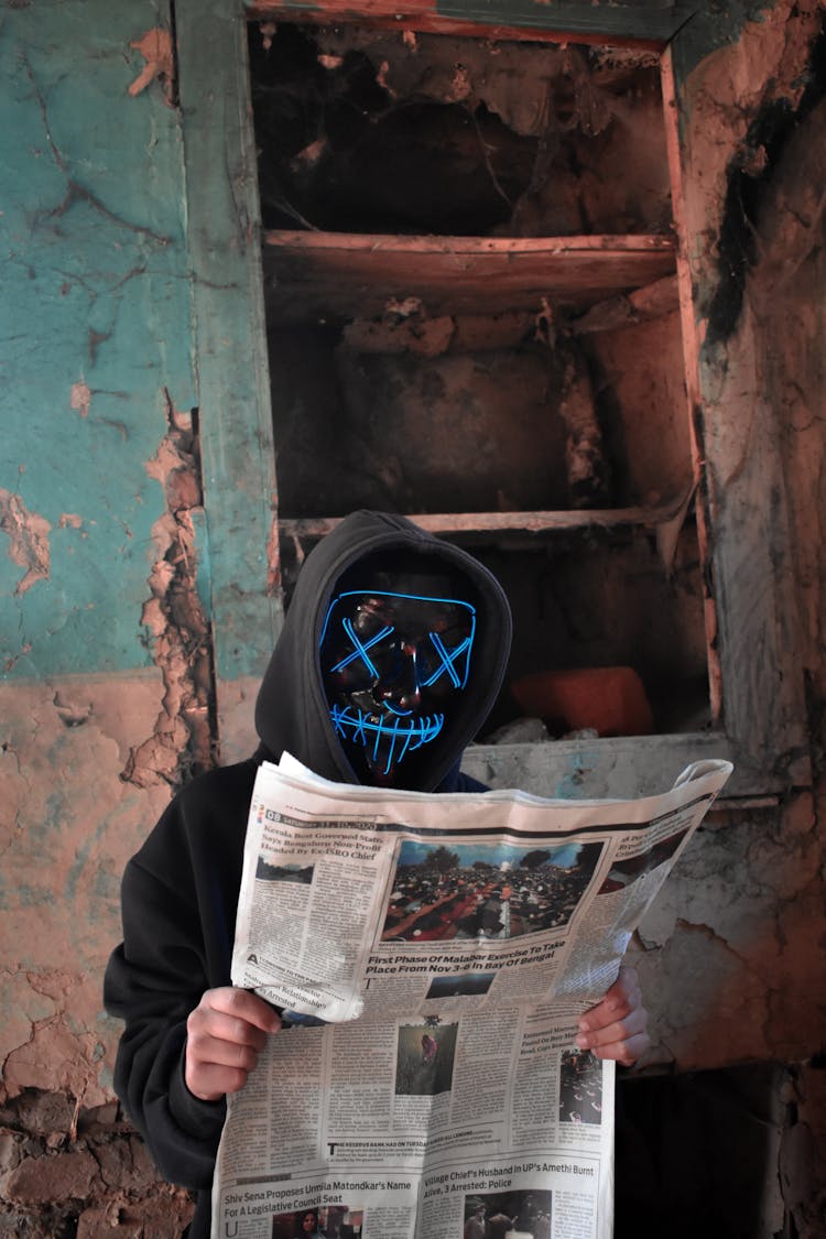 Man With A Mask On Sitting In An Abandoned Building Reading Newspaper 