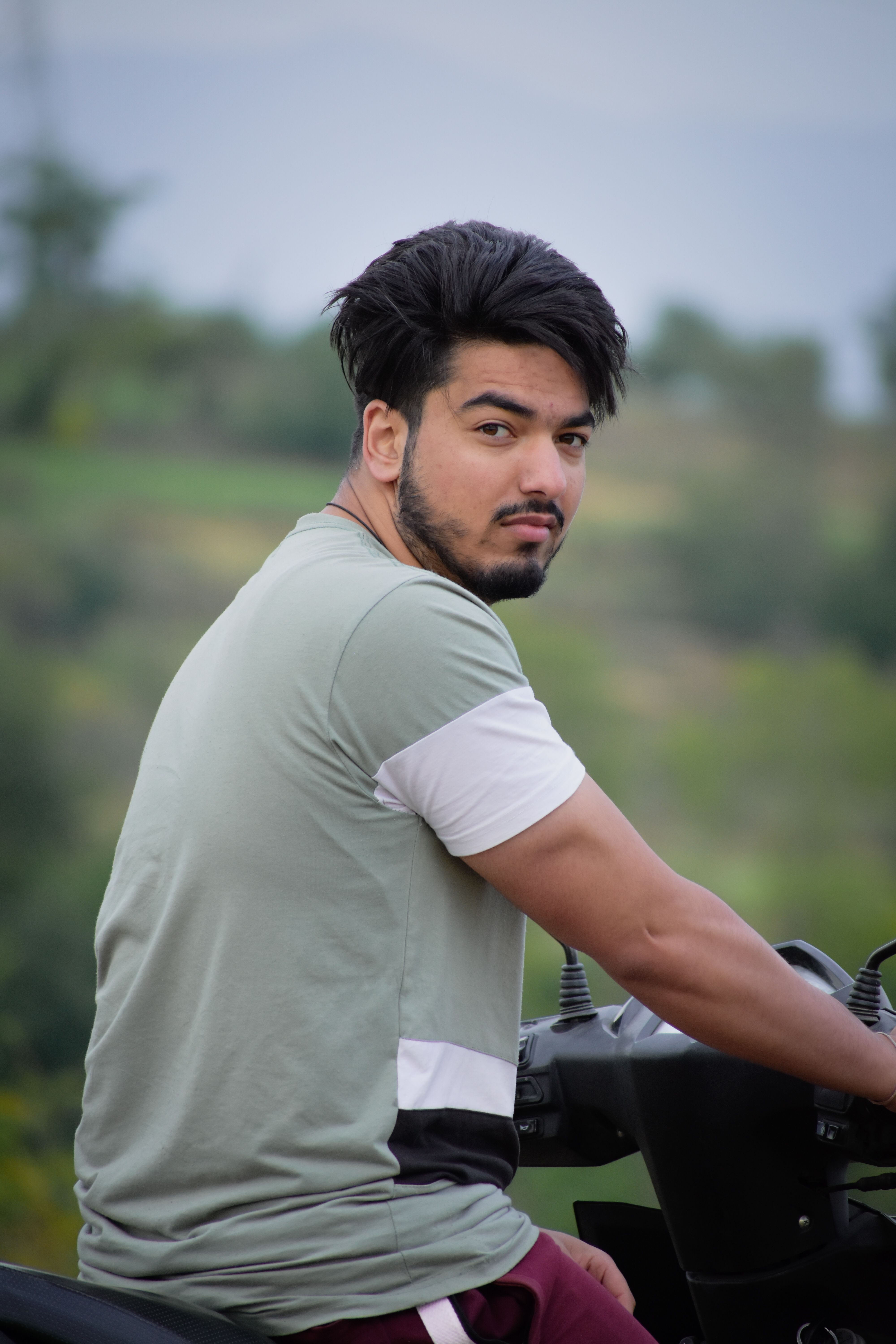 A man sitting on a motorcycle outdoors with a scenic background, looking over his shoulder.