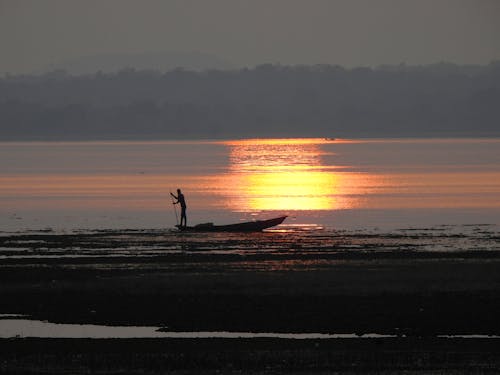 Silhouette of a Person Standing on Boat on the Beach during Sunset