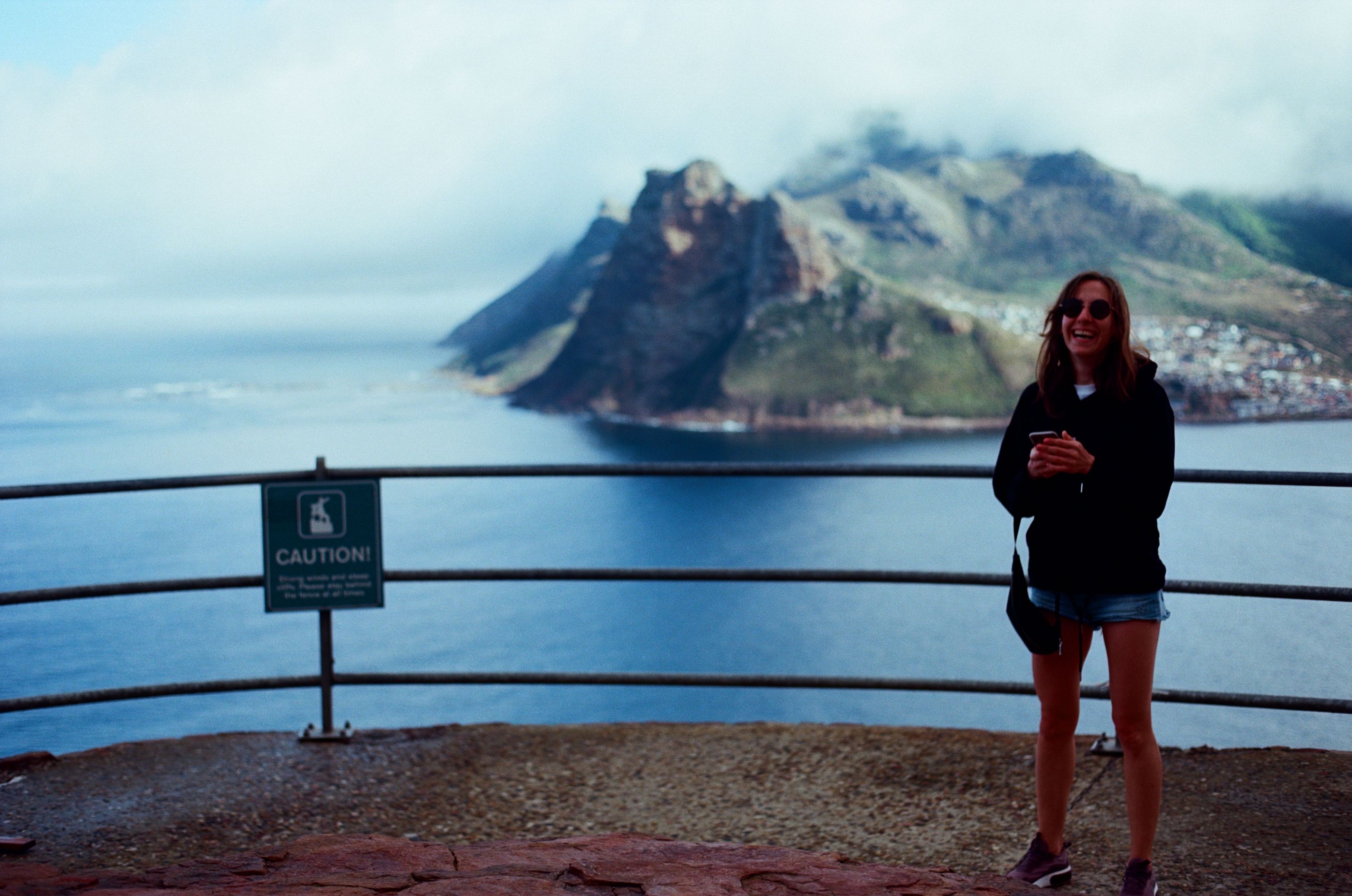 Smiling woman in denim shorts and sunglasses by the ocean in South Africa.
