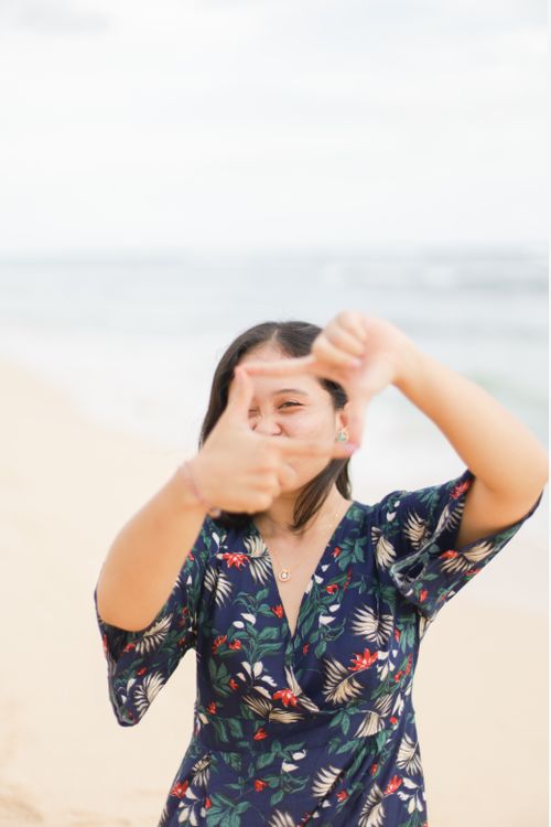Free Young Asian woman in floral top showing thumbs up and thumbs down gestures at the beach. Stock Photo
