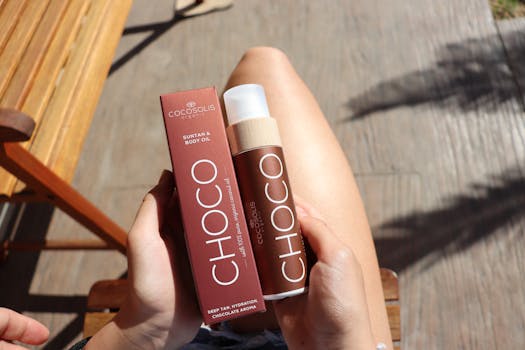 Hands holding Choco Suntan Body Oil while sitting outdoors in sunlight.