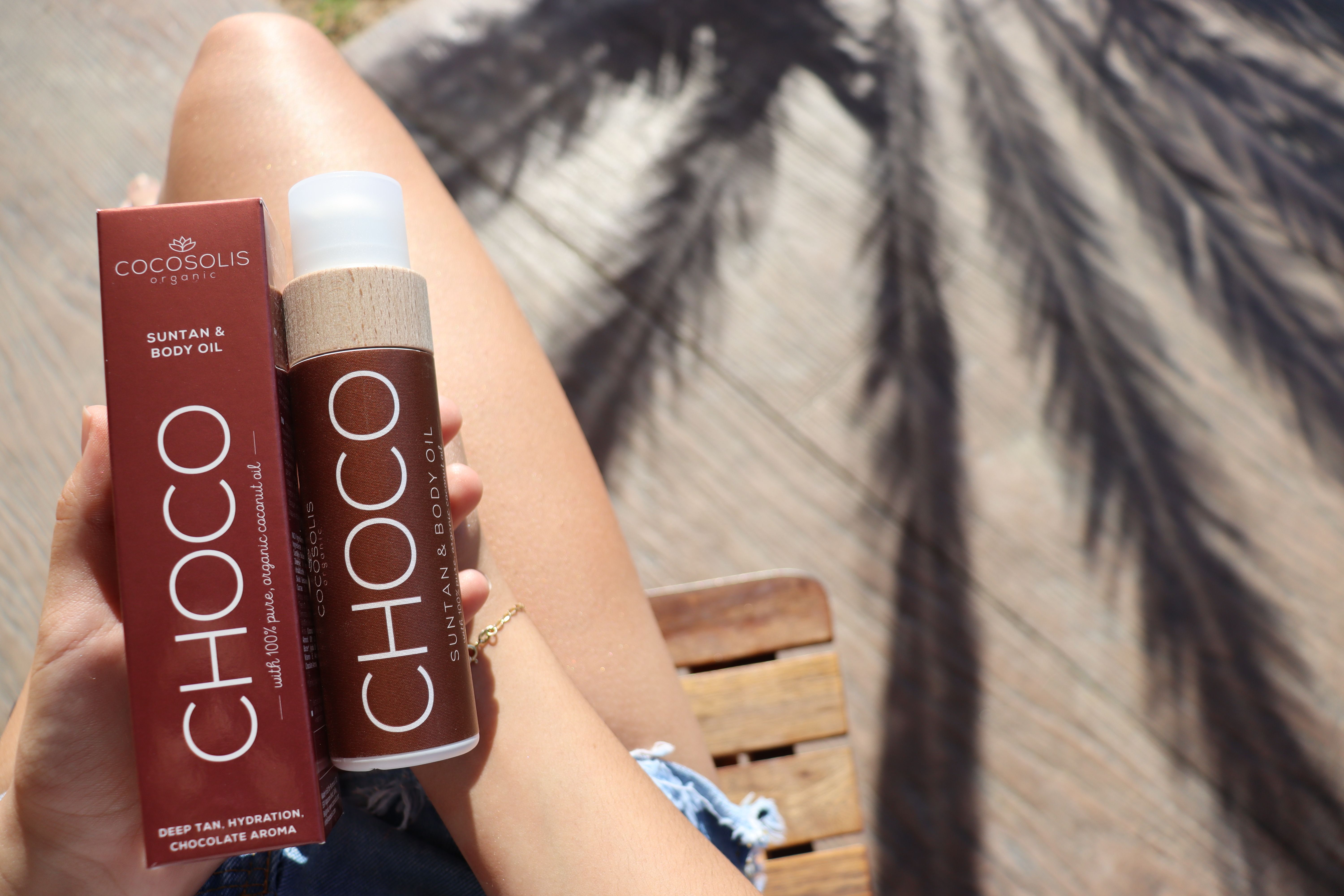 Close-up of a person holding Cocosolis Choco suntan and body oil with natural light.