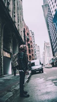 Man stands on the street surrounded by tall buildings in a bustling city.