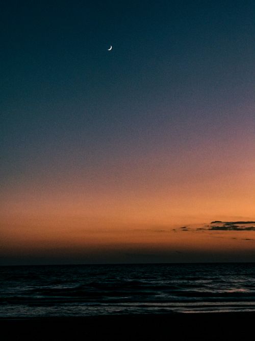Free A peaceful view of the crescent moon above an ocean at twilight, capturing nature's tranquility. Stock Photo