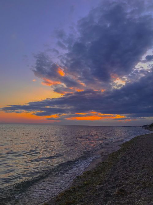 Free A tranquil beach scene at sunset with vibrant colors and dramatic clouds. Stock Photo