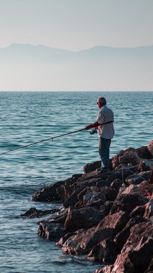 Free A man fishing on the rocks by the sea in Kuşadası, capturing a serene hobby moment. Stock Photo