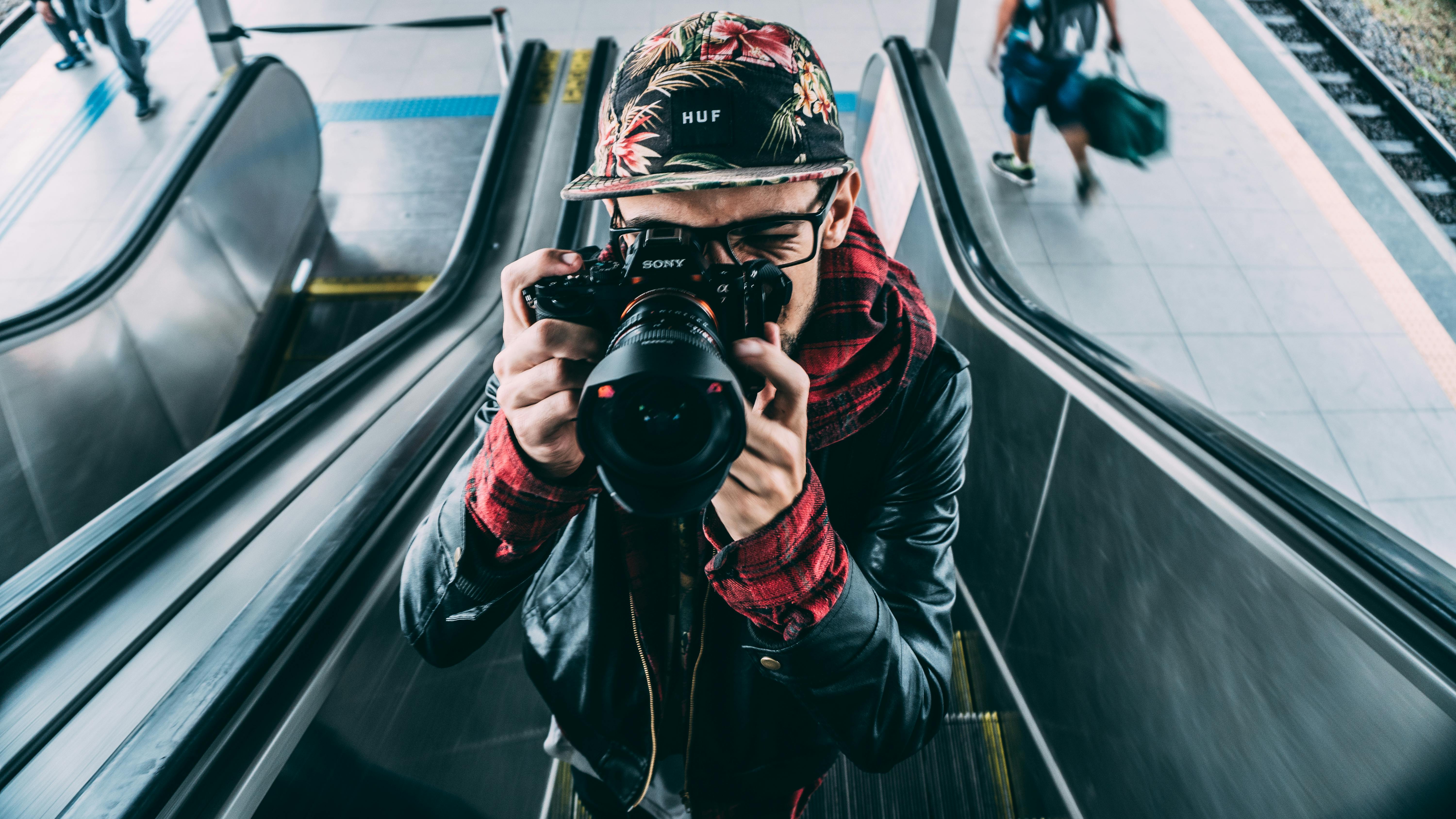 Young man with camera capturing urban scene on an escalator.