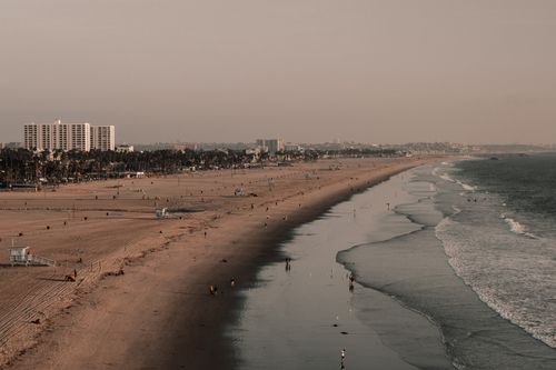 Free Drone shot of expansive beach, city skyline, and calm ocean waves at dusk. Stock Photo