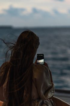 Back view of a woman taking a photo of the ocean with her smartphone.