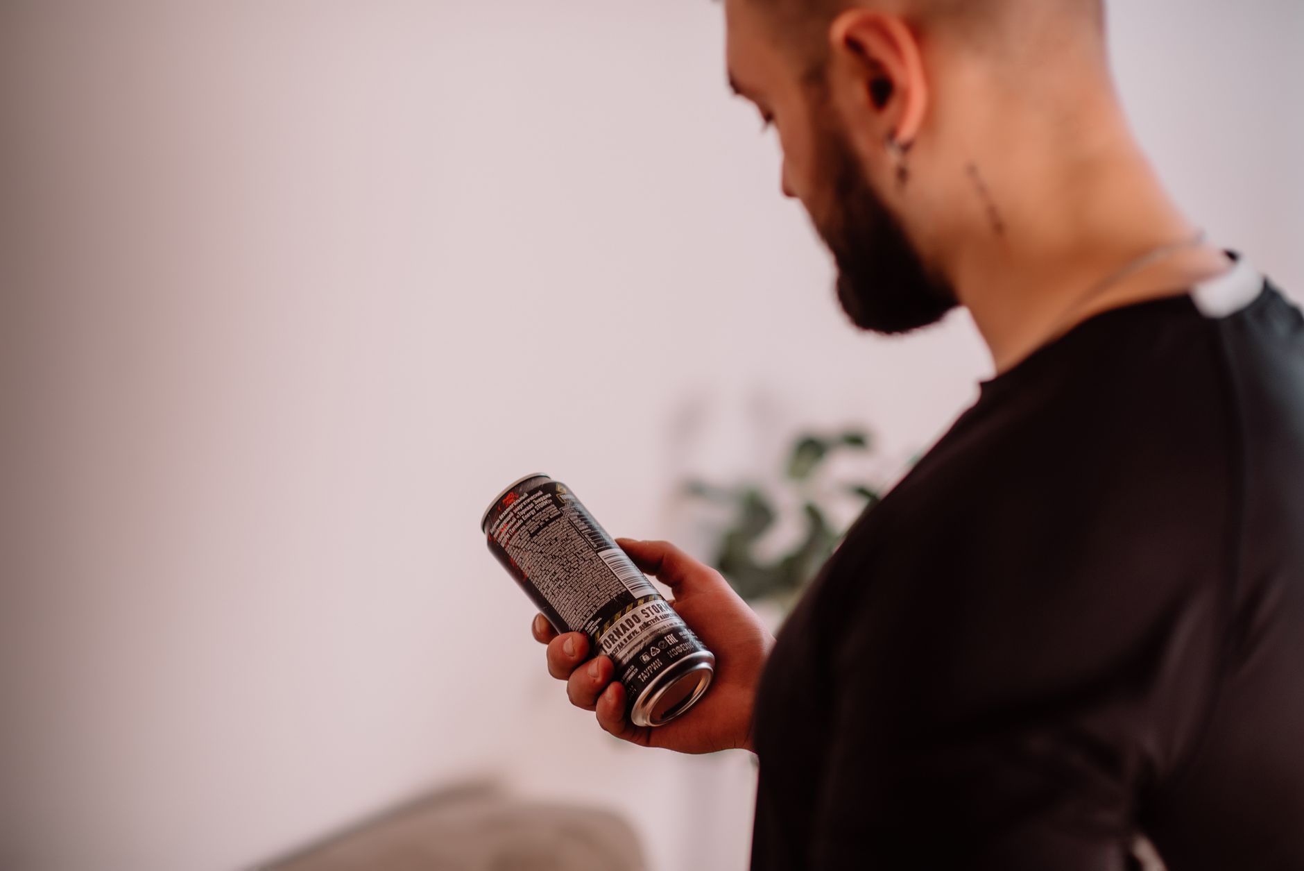 Man examining a drink can indoors with focus on the product label.
