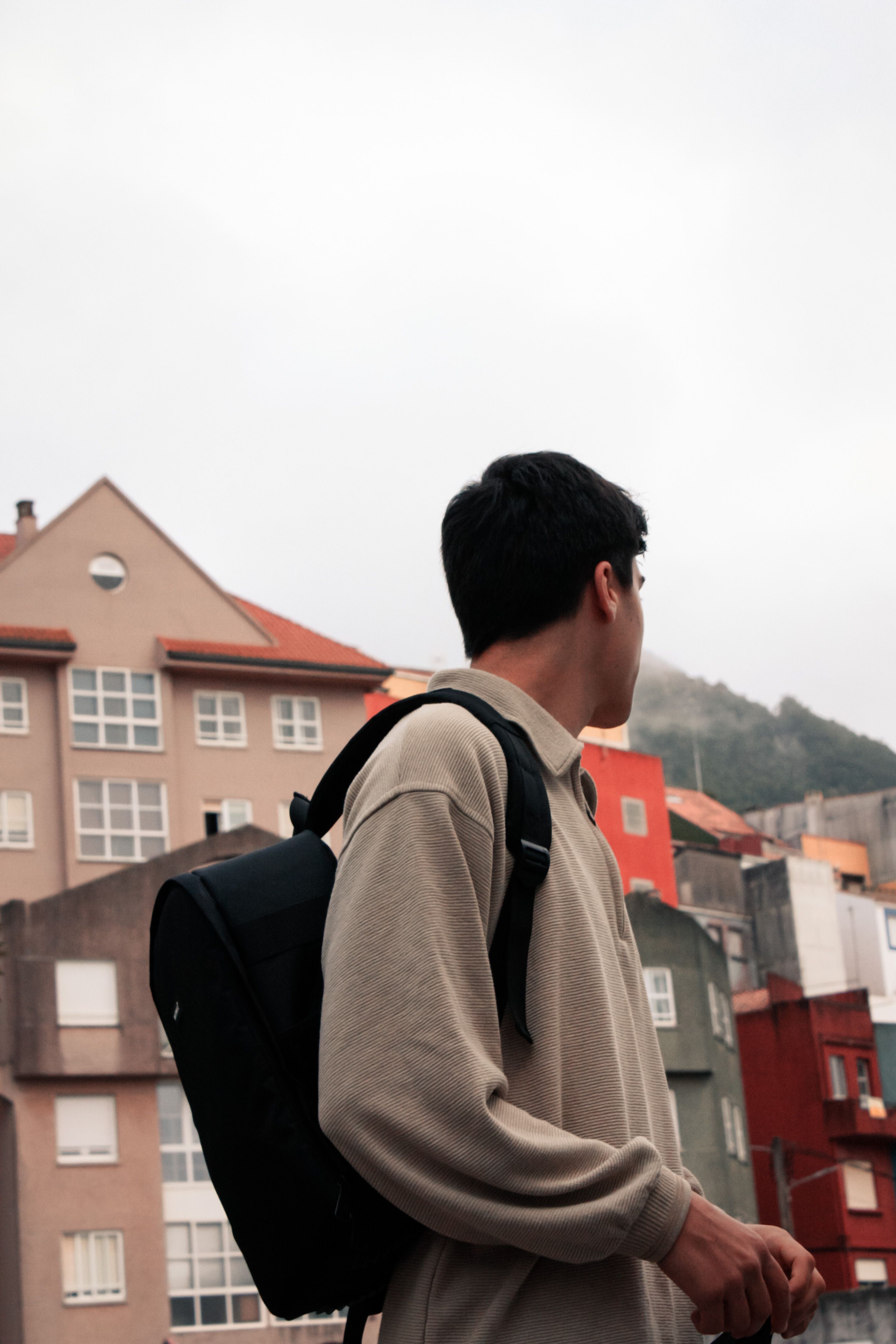 Man in a hoodie with backpack observing urban architecture outdoors.