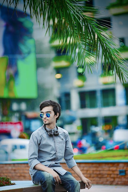 Stylish young man sitting in a vibrant urban park, wearing sunglasses and headphones.