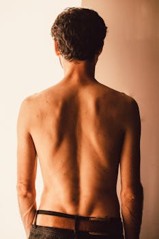 Artistic image of a shirtless man from behind, showcasing defined back muscles in warm lighting.