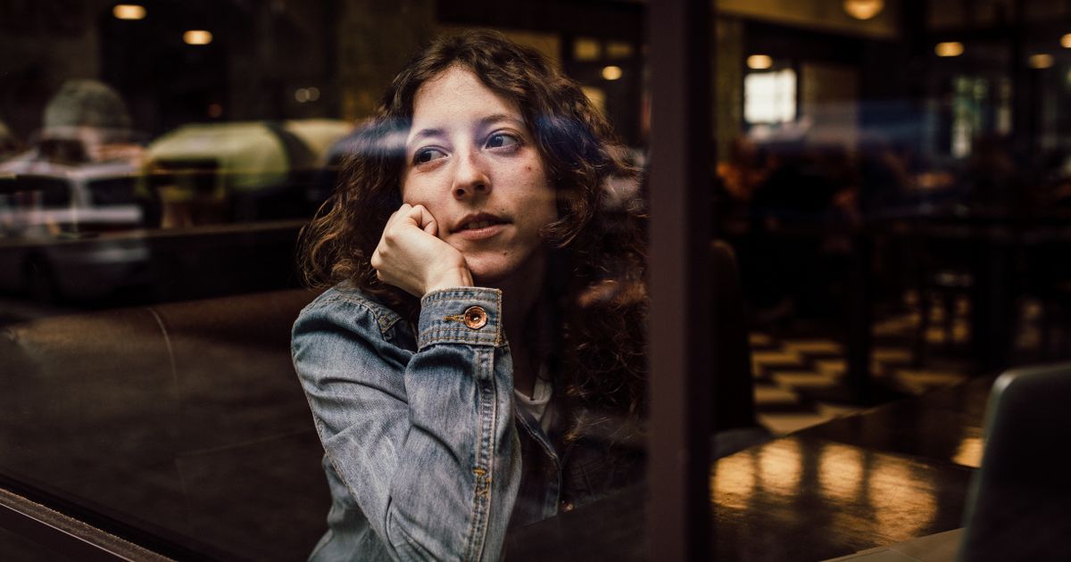 A person standing quietly by a window, appetite gone