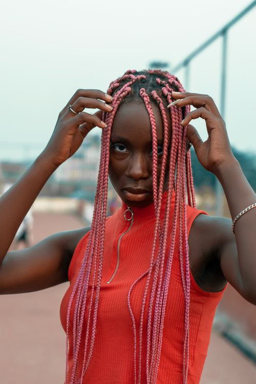 Free A fashionable young woman with vibrant braided hair posing outdoors on a casual day. Stock Photo