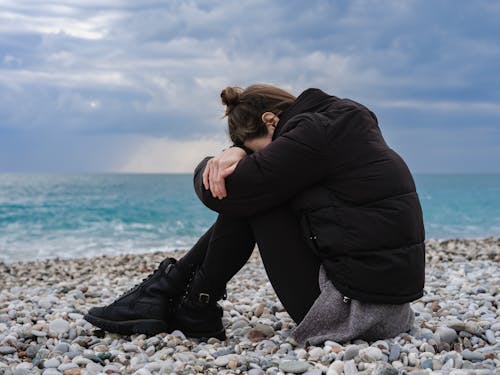 Free Woman Wearing Jacket Sitting on Rocky Shore Stock Photo