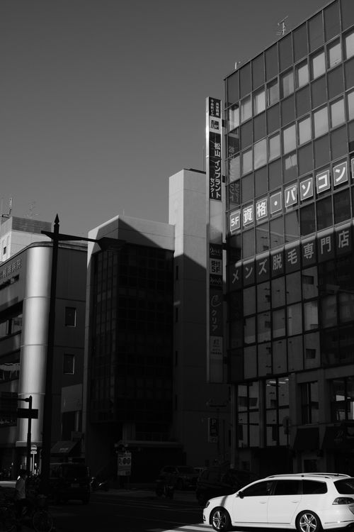 Free Black-and-white photo of urban buildings with a car, showcasing architectural details in city environment. Stock Photo