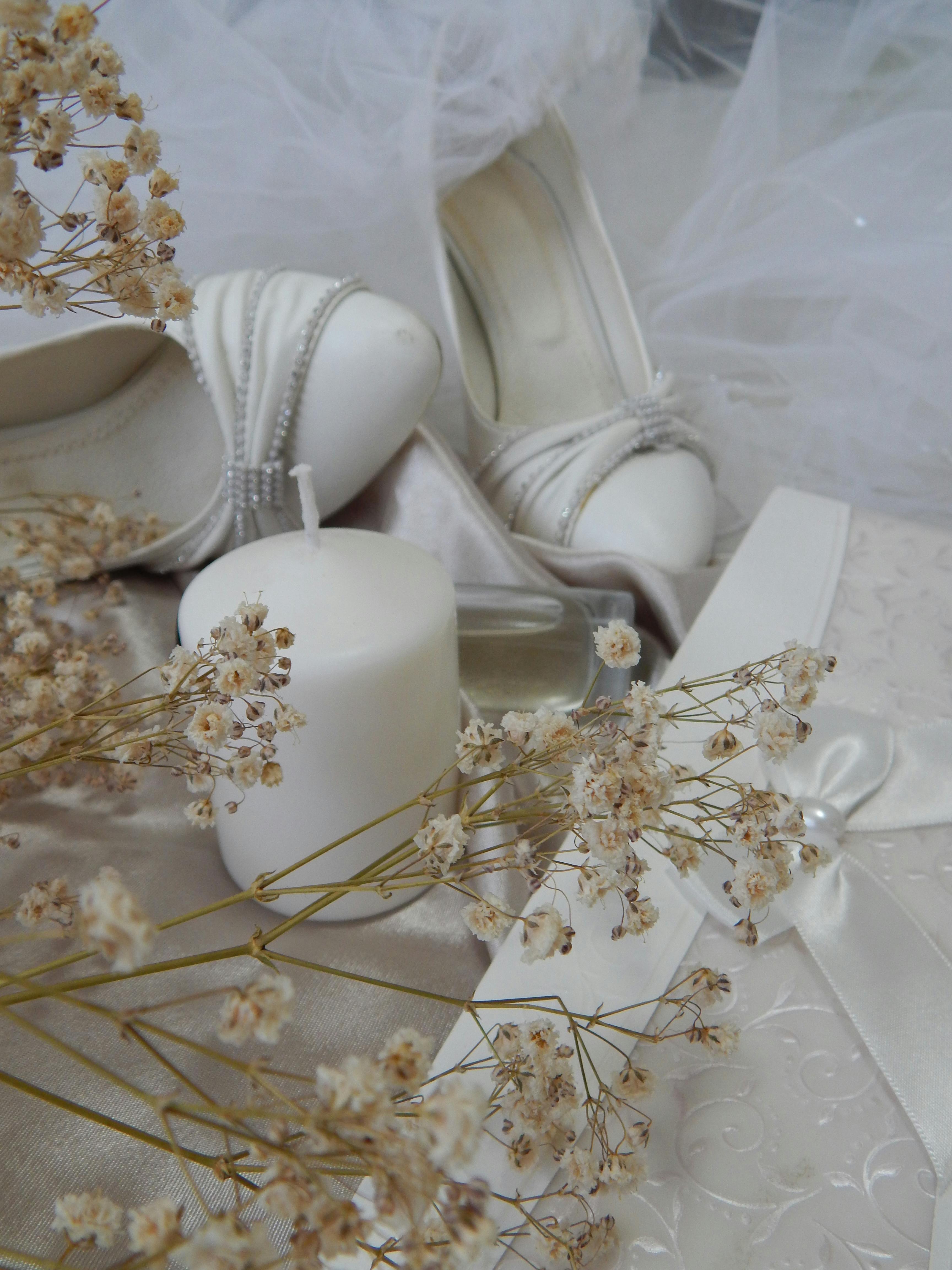 Delicate wedding still life featuring white heels, candle, and dried flowers for elegance.