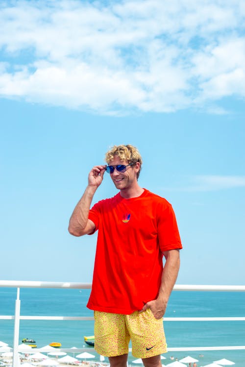 Free Person in Red Shirt Holding Sunglasses Stock Photo