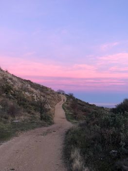 Tranquil dirt path winding through hills with a stunning pink sunset sky.