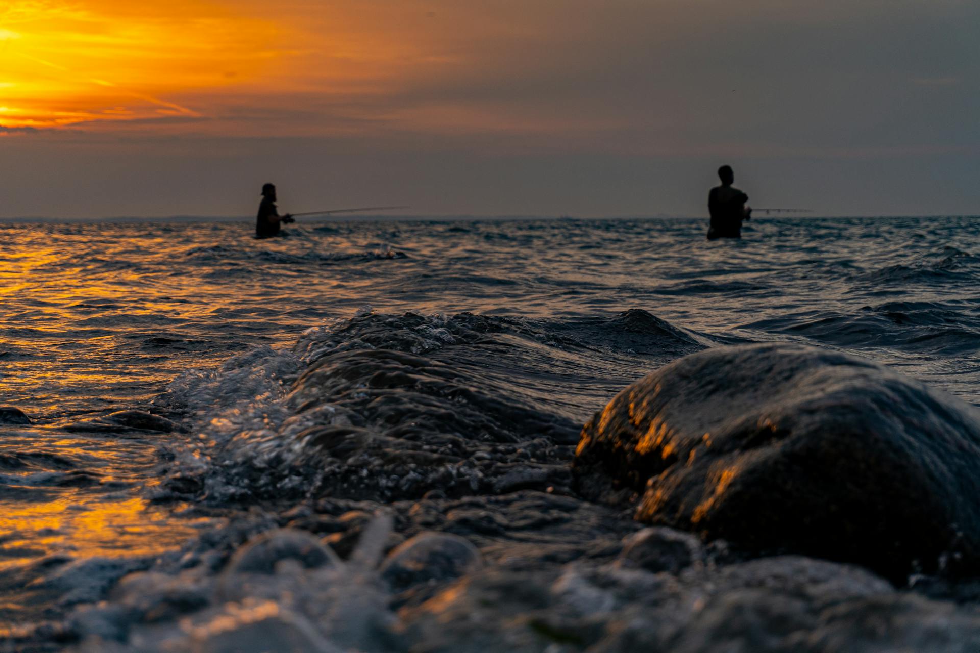 Two fishermen silhouetted against a vibrant sunset, fishing in the Kiel waters.