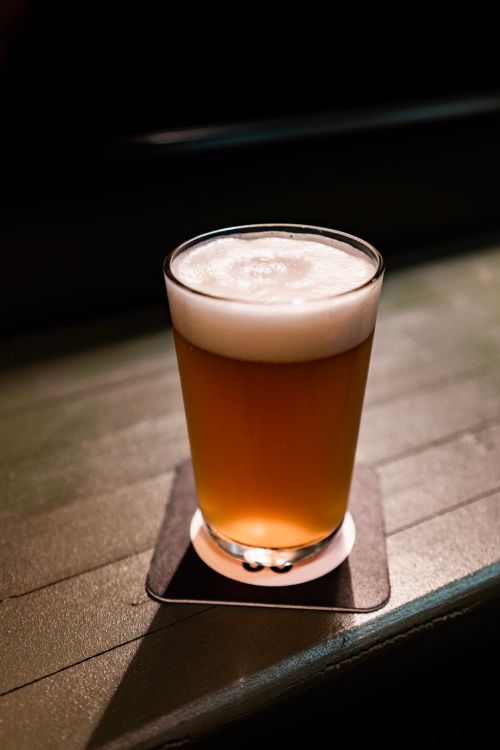 Free A frothy beer in a clear glass resting on a coaster on a wooden table. Perfect for beverage themes. Stock Photo