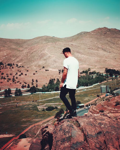 Man in White T-shirt and Black Pants Standing on Cliff