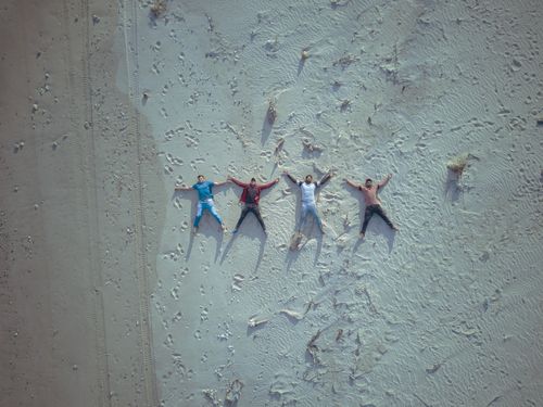 Free Aerial shot of four friends lying on a sandy beach in Port Blair, India. Stock Photo