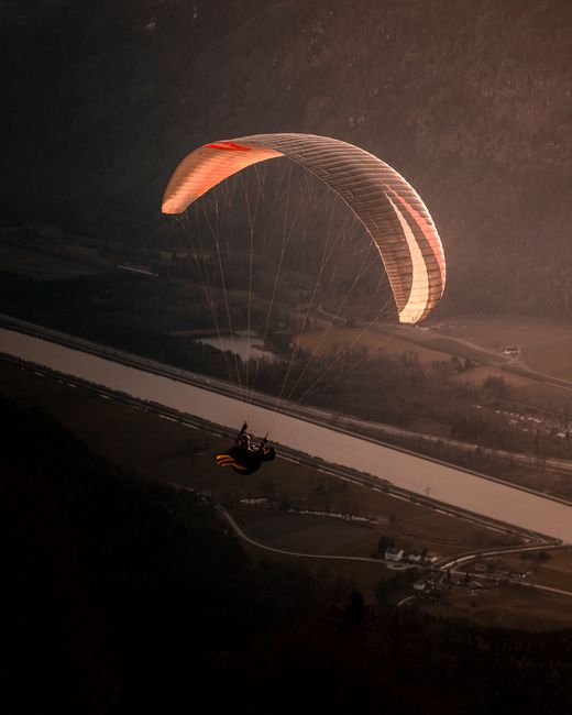 A paraglider soars over the scenic Bavarian landscape during sunset adventure.