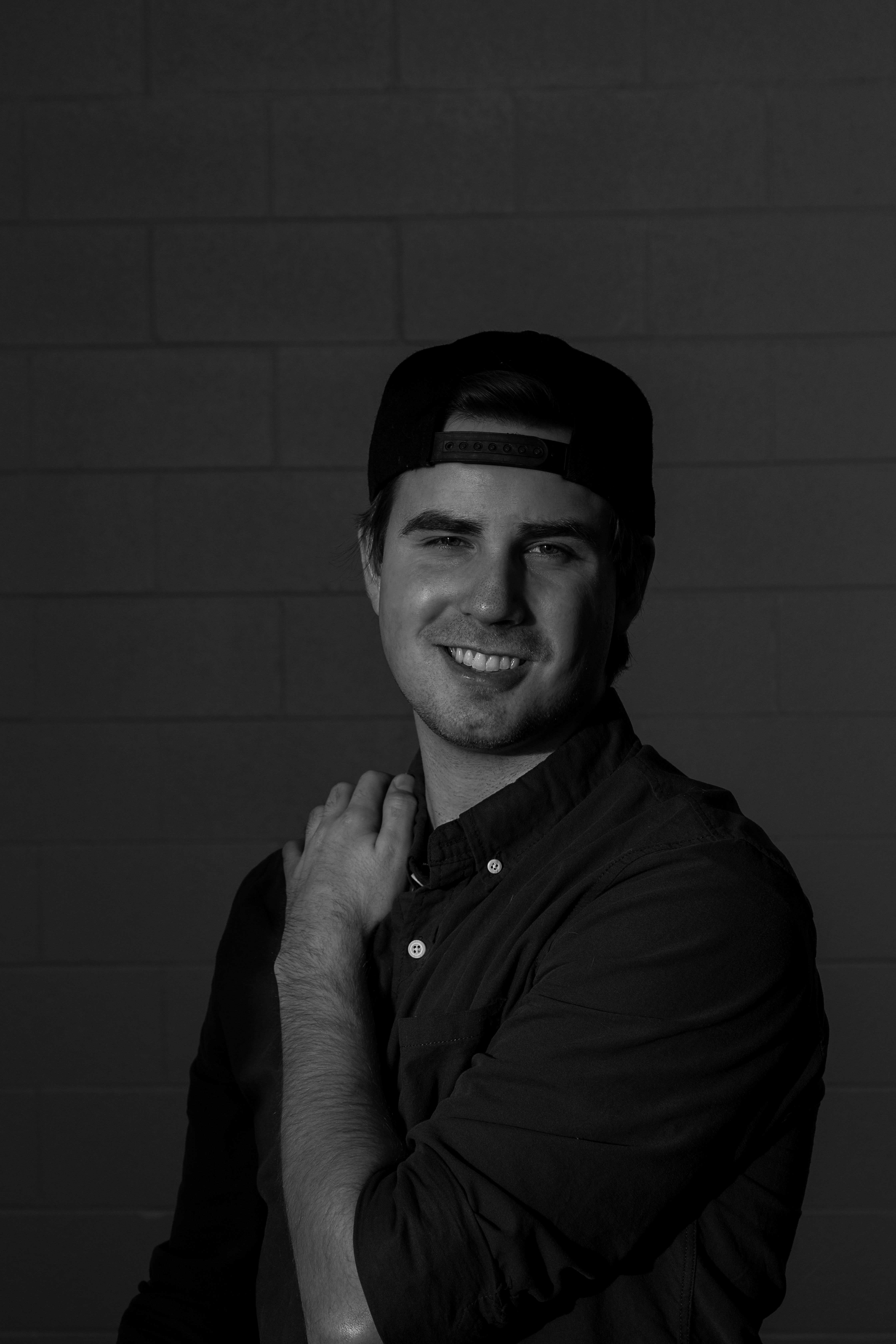 Monochrome portrait of a smiling man in casual attire against a dark background.