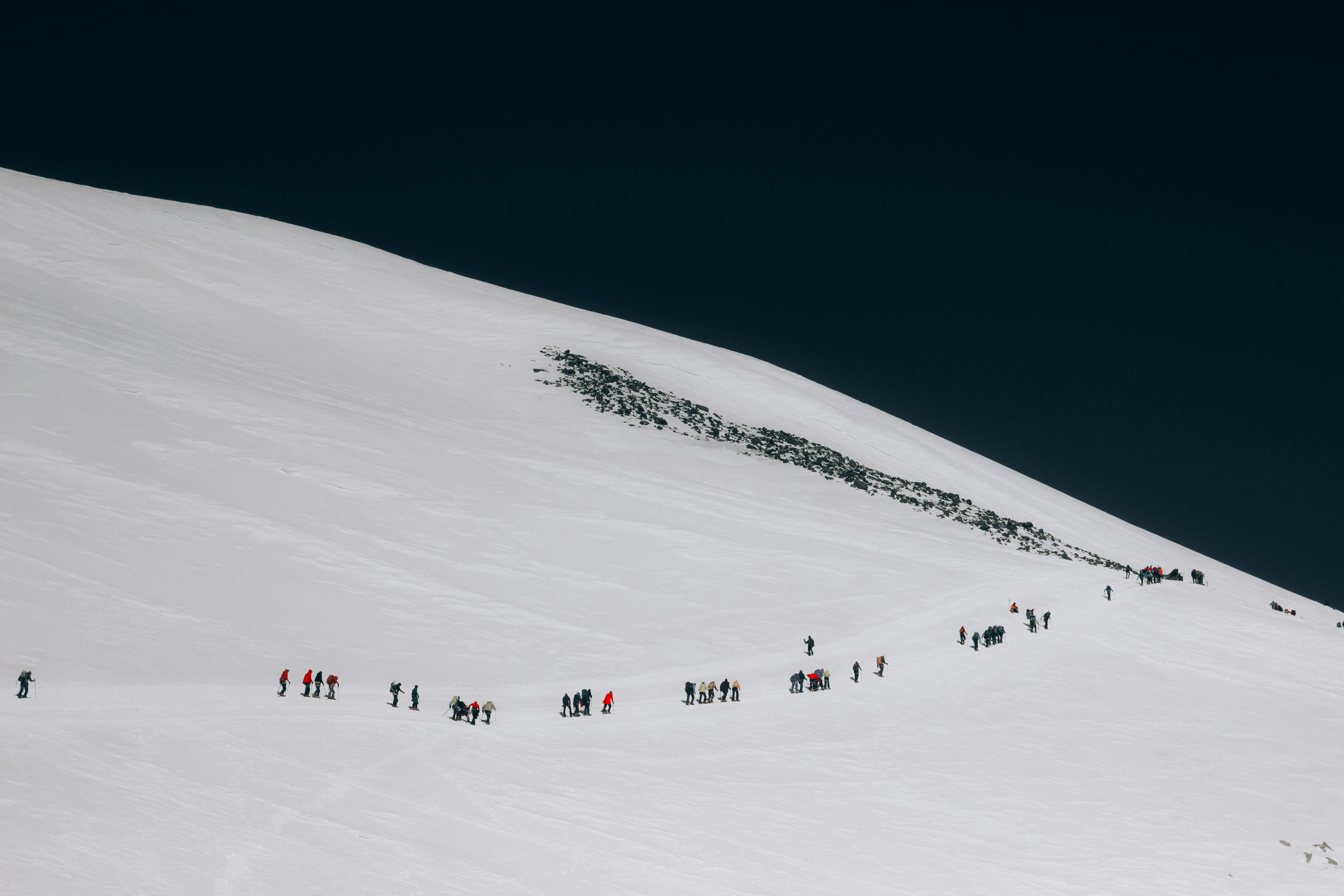 Prescription Goggle Inserts - Adventurous group trekking across a snow-covered mountain slope under a clear sky.