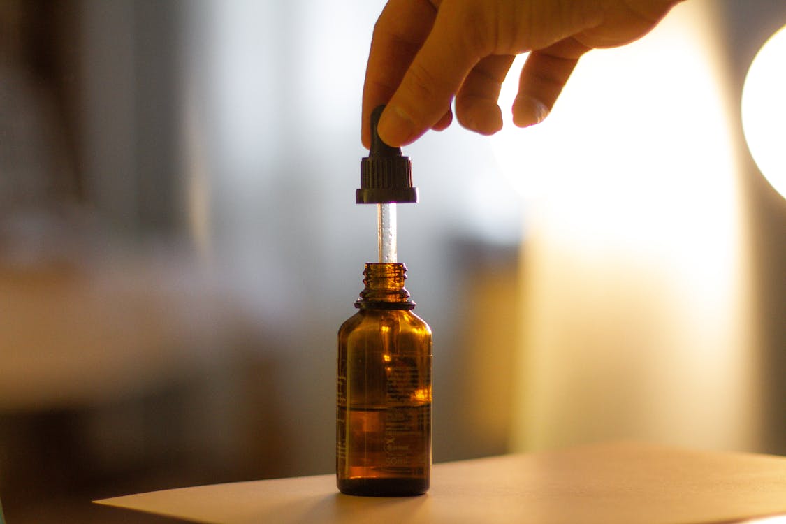 Free A hand holding a serum dropper over a brown glass bottle with a blurred background. Stock Photo