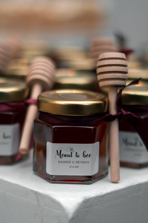 Free Close-up of honey jars tied with ribbons, accompanied by honey dippers, labeled 'Meant to Bee'. Stock Photo