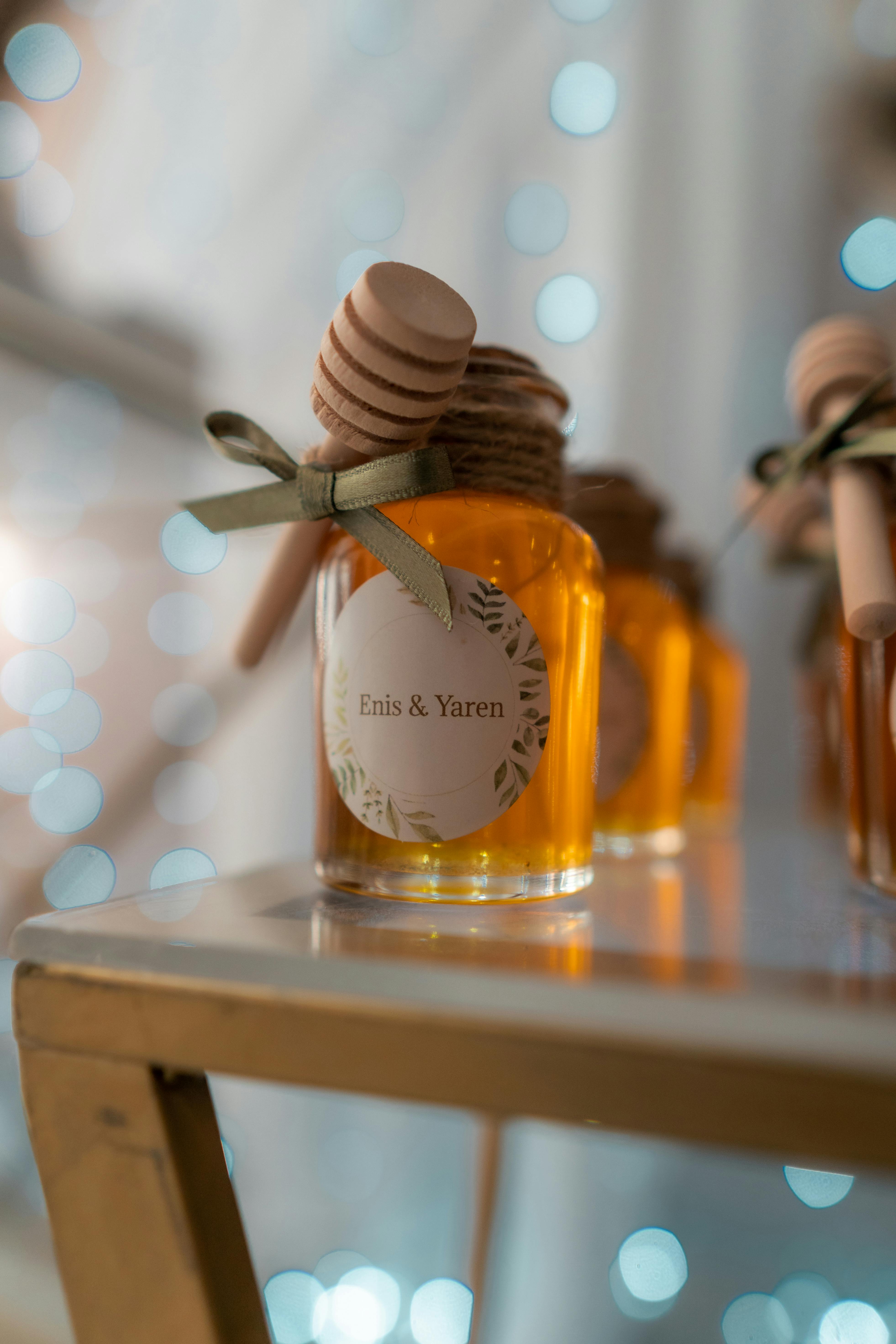 Close-up of a decorated honey jar with a ribbon and wooden dipper against bokeh lights.