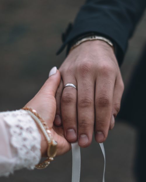 Free A closeup of newlywed couple holding hands, showcasing their wedding rings. Stock Photo
